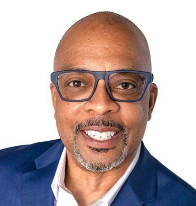 Smiling man with glasses, a goatee, and a shaved head—Kevin M. Yates—wears a blue suit jacket and white shirt, posed against a white background. - Cognota